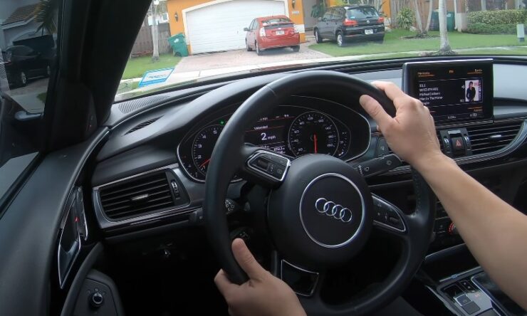 Driver's perspective inside a luxury Audi, hands lightly gripping the steering wheel